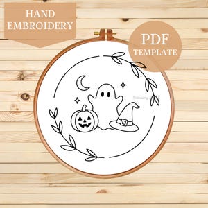 May include: A wooden embroidery hoop containing white fabric with a black line art design featuring a ghost, a jack-o'-lantern, a witch hat, a crescent moon, and stars, framed by a leafy vine. The text HAND EMBROIDERY and PDF TEMPLATE appear.