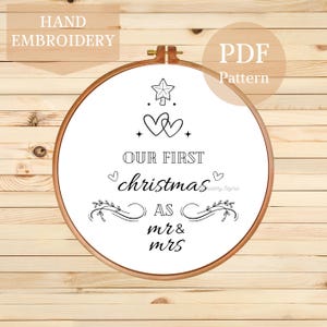 May include: Black and white embroidery pattern for a hoop featuring a stylized Christmas tree with two hearts at the base and the text "Our First Christmas as Mr & Mrs".
