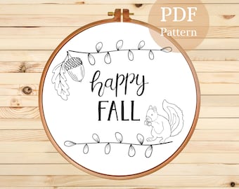 Puede incluir: Patrón de bordado en blanco y negro con una ardilla sosteniendo una bellota, una rama con hojas y el texto "happy fall".