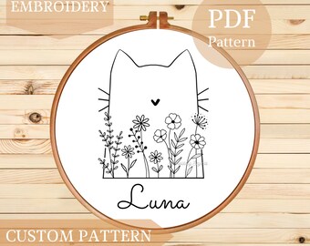Może przedstawiać: Wzór haftu czarno-białego w postaci linii przedstawiający kota z kwiatami i imieniem "Luna" w obręczy.