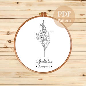 May include: A black and white line drawing of a gladiolus flower in a hoop. The text "Gladiolus August" is below the flower.