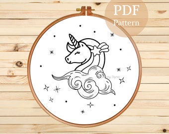 May include: A black and white line drawing of a unicorn with a star on its head, sleeping on a cloud with stars around it. The drawing is in a hoop, and the text "PDF Pattern" is above the hoop.