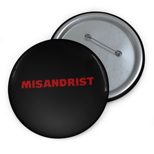 May include: A black button with a red, jagged text that reads "MISANDRIST". The button has a silver back.