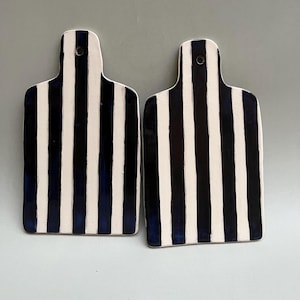 Könnte beinhalten: Zwei Keramik-Schneidebretter mit einem schwarz-weißen Streifenmuster. Die Streifen sind in dunkelblau lackiert.
