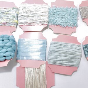 May include: Assortment of blue, white and silver ribbon spools on pink card stock. The ribbon spools are arranged in two rows.