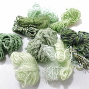 Op de afbeelding: Assortiment van groene garenklossen in verschillende tinten en texturen, waaronder een klos met een blauw-groen gestreept patroon.