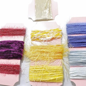 Puede incluir: Surtido de carretes de hilo de colores sobre cartulina rosa. Los colores del hilo incluyen rojo, morado, amarillo, azul y blanco.