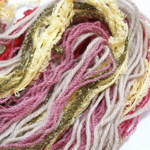 Peut inclure: Gros plan sur un écheveau de fil de couleur beige, rose, jaune et or. Le fil est doux et moelleux, et il a un aspect légèrement texturé.