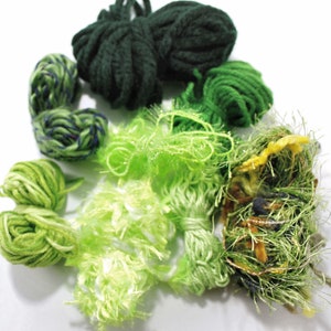 May include: Assortment of green yarn in various textures, including a fluffy, a chunky, and a smooth yarn. The yarn is arranged in a circle on a white background.