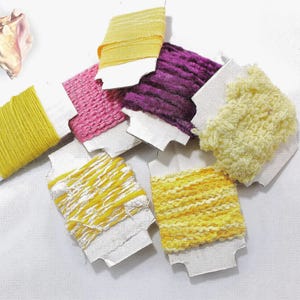 Peut inclure: Assortiment de bobines de fil de différentes couleurs et textures, y compris lisse, duveteux et texturé, sur un fond blanc.