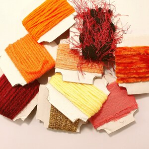 May include: Assortment of colorful embroidery floss spools in various shades of orange, red, and yellow. The floss is wound on white cardboard spools.