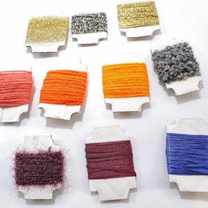 Può includere: Assortimento di rocchetti di filo colorati su cartoncino bianco. I colori del filo includono arancione, rosa, viola, blu, grigio, oro e argento.