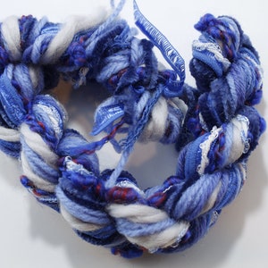 Peut inclure: Une pelote de laine bleue, blanche et rouge avec un ruban tissé à travers elle. La laine est douce et moelleuse, et le ruban est soyeux et lisse.