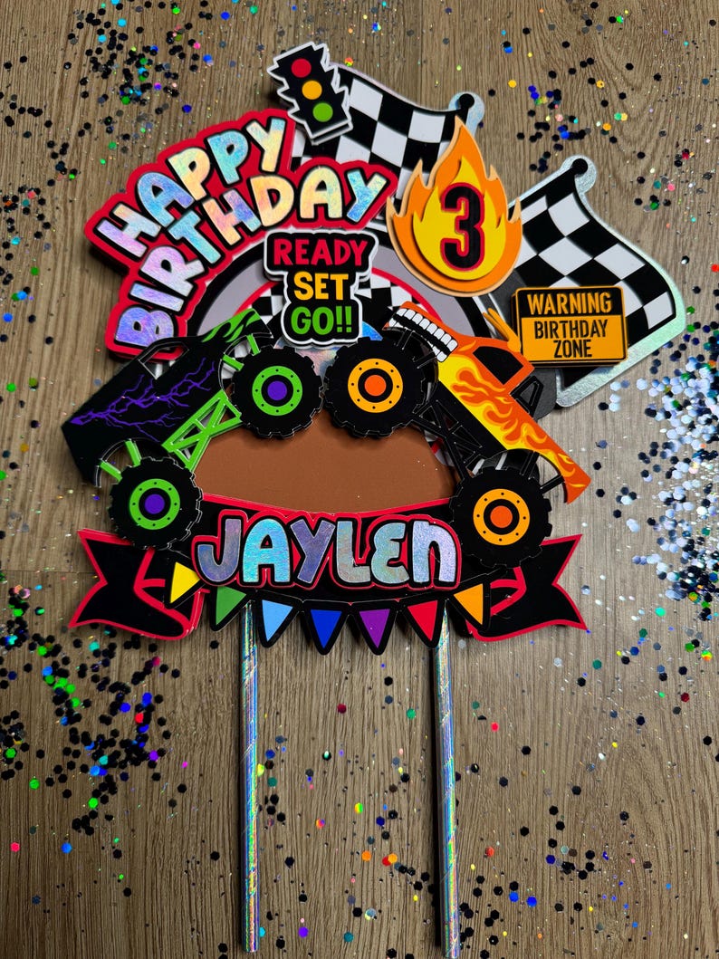 May include: A colorful monster truck themed cake topper with the words "Happy Birthday", "Ready Set Go!" and "Jaylen". The topper also includes a checkered flag, a traffic light, a number 3, and a sign that says "Warning Birthday Zone".