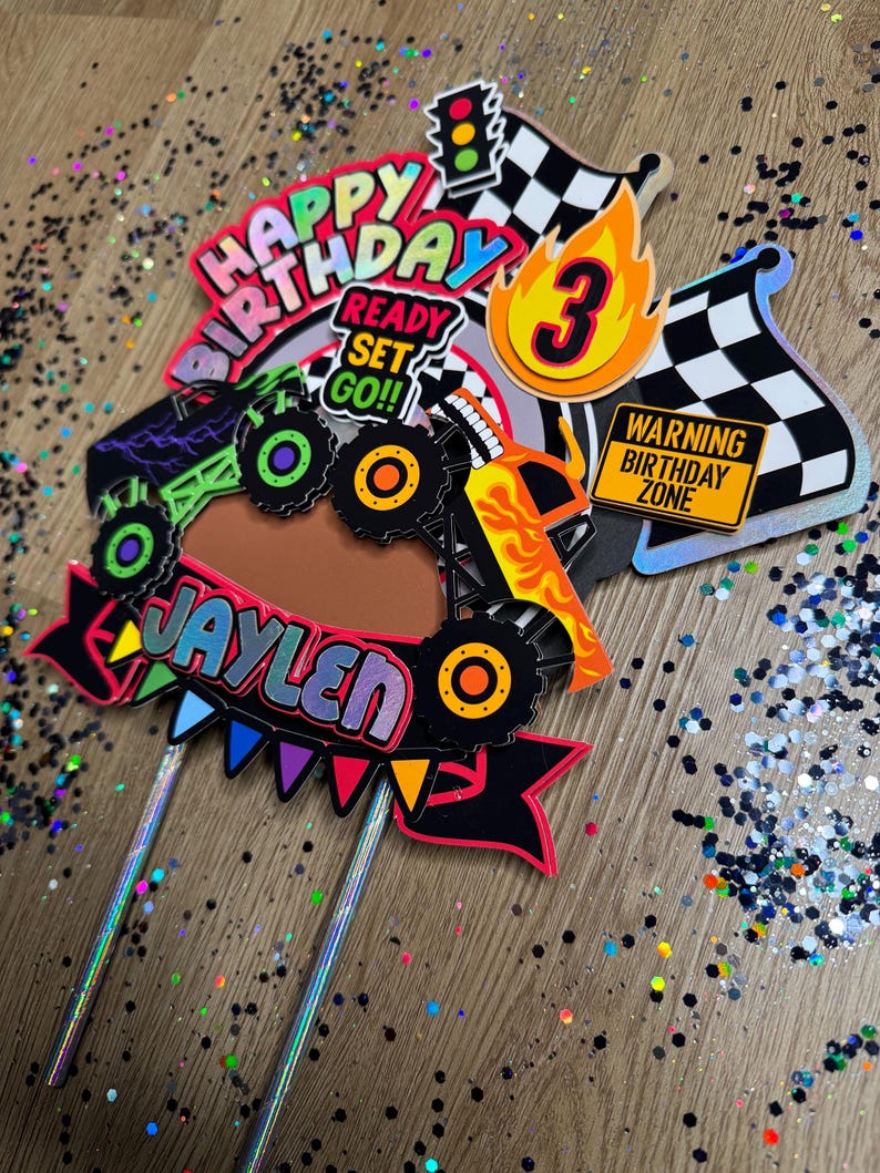 May include: A monster truck cake topper with a red, yellow, and black monster truck, a red and yellow banner that says "Happy Birthday", a red, yellow, and blue banner that says "Ready Set Go!!", a yellow and orange banner that says "Jaylen", a yellow and orange number 3, a red and white checkered flag, a red and white checkered flag with a yellow flame, and a yellow sign that says "Warning Birthday Zone".