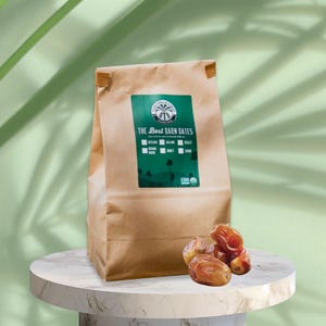 May include: A brown paper bag of dates with a green label that reads "The Best Darn Dates." Several dates are in front of the bag. The label lists date varieties. The background is a light green with a marble-like surface.