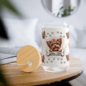 Puede incluir: Una lata de vidrio blanca con tapa y una pajita. La lata tiene un diseño de un Yorkshire Terrier con un lazo rosa y el texto "Yorkie Mom".