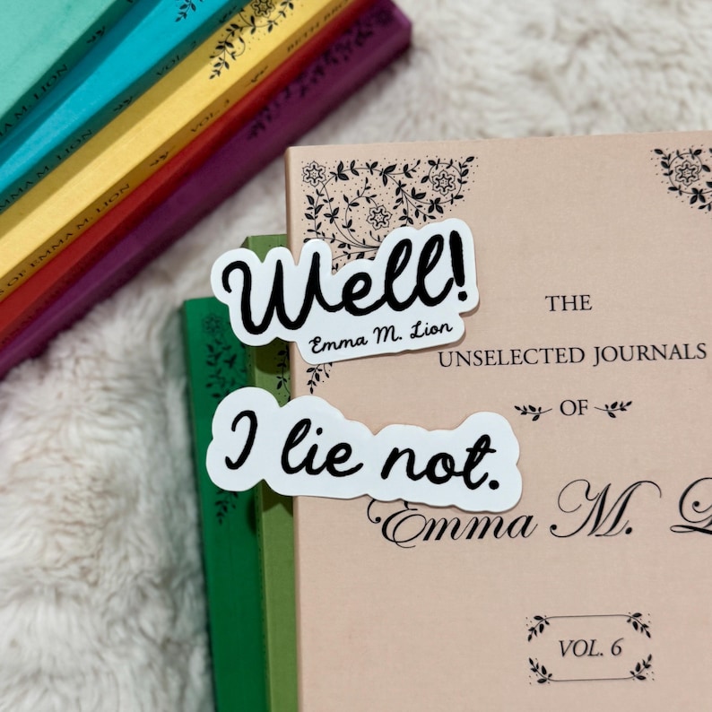 Op de afbeelding: Twee witte stickers met zwarte tekst liggen op een boek. E&eacute;n sticker zegt "Well!" en "Emma M. Lion". De andere sticker zegt "I lie not." Verschillende boeken met kleurrijke ruggen zijn op de achtergrond.
