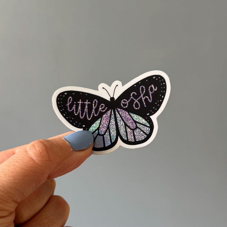 May include: A black butterfly sticker with iridescent wings and the text "little oshq" in purple glitter.