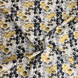 Könnte beinhalten: Stoff mit einem sich wiederholenden Blumenmuster. Das Design zeigt stilisierte Blumen und Blätter in Schwarz, Gold und Grau auf cremefarbenem Hintergrund. Vertikale Reihen mit schwarzen Blattgruppen und goldenen Blütenformen.