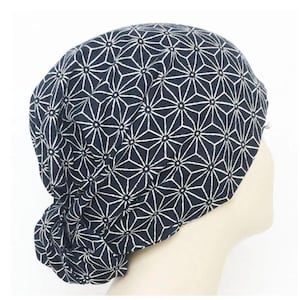 Può includere: Un cappello a fantasia blu navy e bianco. Il cappello presenta un motivo geometrico a stella ripetuto. Il tessuto è morbido e sembra leggero. Il cappello è mostrato su una testa di manichino.