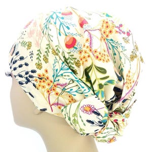 Peut inclure: Un turban crème orné d'un motif floral vibrant. Le design comprend des fleurs colorées, des feuilles vertes et des tiges dans des tons de jaune, rose et bleu. Le turban est noué sur le côté, mettant en valeur le motif complexe du tissu.