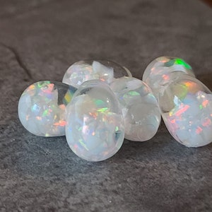 May include: A group of six iridescent white opal cabochons, each with a unique pattern of color and light.