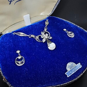 May include: A silver necklace and earrings set with a teardrop-shaped opal pendant and a floral design. The jewelry is displayed in a blue velvet box with a "Sterling Silver Genuine Opals" label.