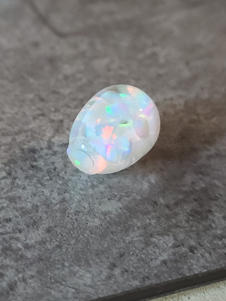 May include: A white opal gemstone with iridescent colors, shaped like an egg.