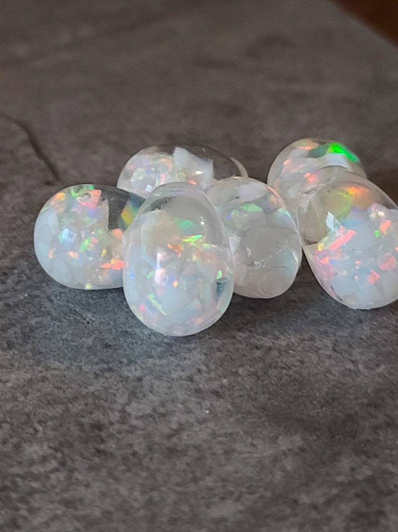 May include: A group of six iridescent white opal cabochons, each with a unique pattern of color and light.
