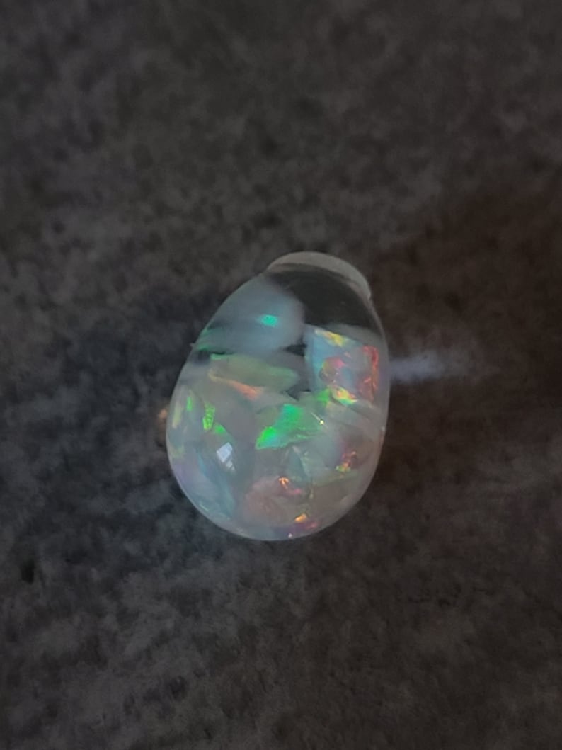 May include: A teardrop-shaped opal pendant with a white base and iridescent green, blue, and pink flashes.