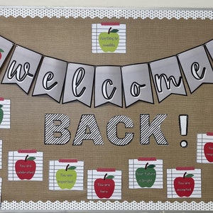 Puede incluir: Un tablero de anuncios marrón con una pancarta de bienvenida con manzanas rojas y las palabras "welcome" en cursiva blanca. El tablero también tiene una pancarta a rayas blanco y negro con la palabra "BACK!" en blanco. Hay varias tarjetas pequeñas con manzanas rojas y mensajes positivos en ellas.