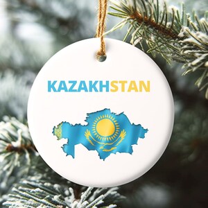 May include: White ceramic Christmas ornament with a blue and yellow map of Kazakhstan and the word "KAZAKHSTAN" printed in black.