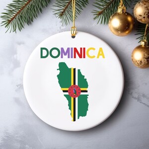 May include: A white ceramic Christmas ornament with a green, yellow, and black outline of Dominica and the word "DOMINICA" in colorful letters.