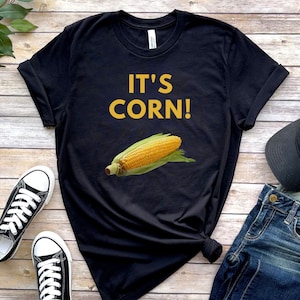 May include: Black t-shirt with the text "IT'S CORN!" in yellow letters and a cartoon image of a corn cob on a black background.