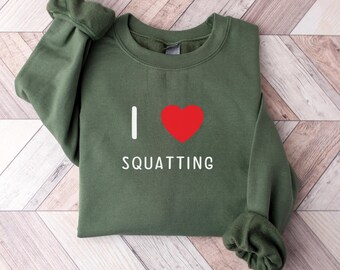 May include: Green sweatshirt with a white graphic that says "I love squatting" with a red heart.