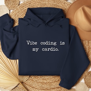 May include: A navy blue hooded sweatshirt featuring the white text "Vibe coding is my cardio." printed on the front. The garment includes a hood with matching drawstrings, long sleeves, and a front kangaroo pocket, presented in a flat layout.
