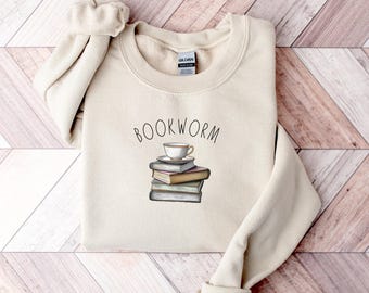 May include: A beige sweatshirt with the text "BOOKWORM" and a graphic of a cup of tea on top of a stack of books.