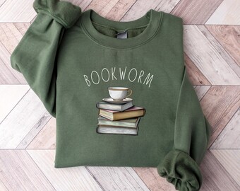 May include: A green sweatshirt with the text "BOOKWORM" printed on the front. The text is in white and is centered on the sweatshirt. There is a small illustration of a cup of tea and a stack of books below the text.