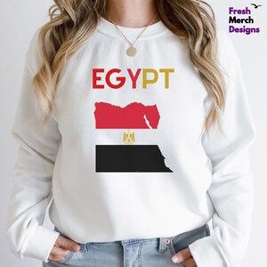 May include: White sweatshirt with the word "EGYPT" in red, yellow, and orange letters. The sweatshirt features a graphic of the Egyptian flag with the country's outline in red and black.