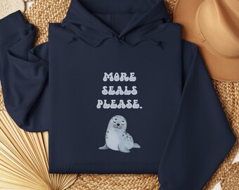 May include: Navy blue hooded sweatshirt featuring the text "MORE SEALS PLEASE." and a cartoon seal illustration. The sweatshirt has a drawstring hood and a front pocket. The design is in white and light blue.