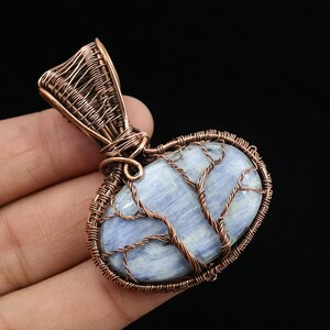 May include: A handcrafted pendant featuring a light blue stone encased in copper wire. The wire is intricately woven around the stone, forming a tree-like design. The pendant has a loop for a chain and is set against a dark background.