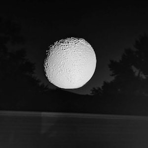 May include: A close-up of the moon in a black and white image. The moon is full and has a textured surface.