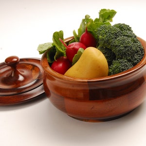 May include: A wooden bowl with a lid, filled with fresh vegetables. The bowl is made of dark wood and has a natural finish. The vegetables include radishes, a yellow potato, and broccoli florets.