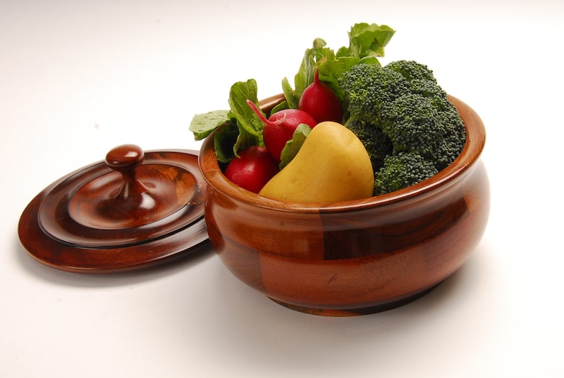 May include: A wooden bowl with a lid, filled with fresh vegetables. The bowl is made of dark wood and has a natural finish. The vegetables include radishes, a yellow potato, and broccoli florets.