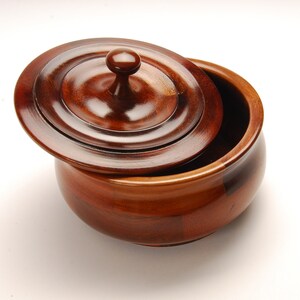 May include: A wooden bowl with a lid. The bowl is made of dark wood with a reddish hue. The lid has a knob on top.