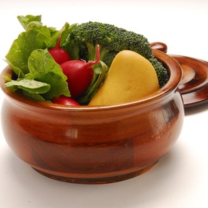 May include: A wooden bowl with a lid, filled with fresh produce. The bowl contains radishes, broccoli florets, and a yellow pear.