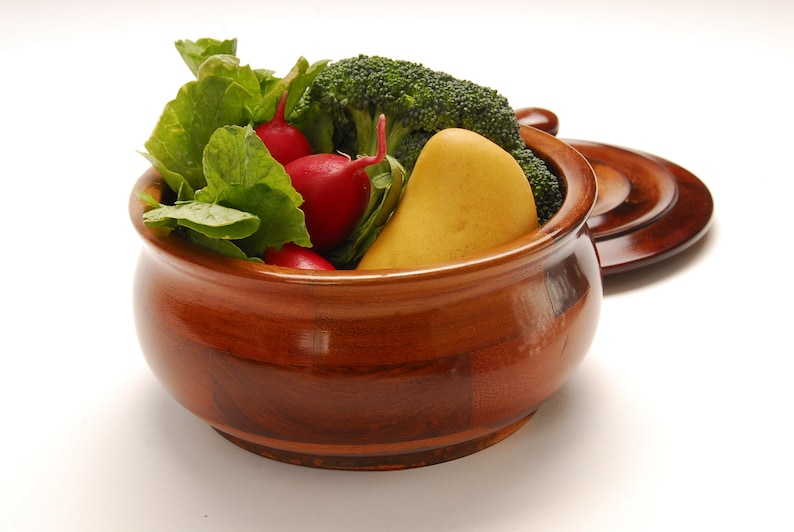 May include: A wooden bowl with a lid, filled with fresh produce. The bowl contains radishes, broccoli florets, and a yellow pear.