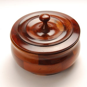 May include: A wooden bowl with a lid. The bowl is made of different types of wood, creating a unique pattern. The lid has a knob on top.