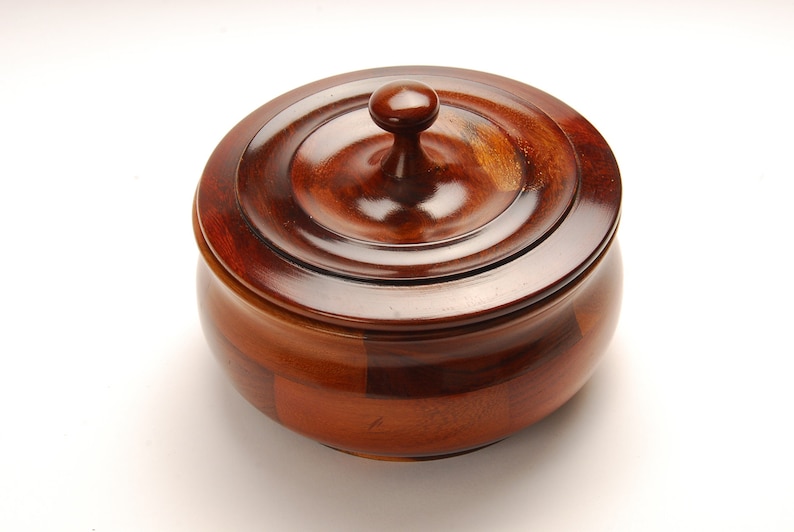 May include: A wooden bowl with a lid. The bowl is made of different types of wood, creating a unique pattern. The lid has a knob on top.